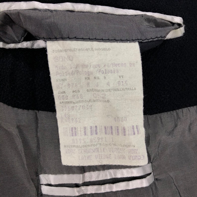 May include: Close-up of a black garment's interior, revealing a tag with text in multiple languages. The tag includes details like "SONG", "Poland/Pologa/Polonia", and various codes and numbers. The lining is gray with white trim.