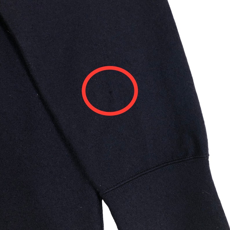 May include: Close-up of a navy blue sweatshirt sleeve. The fabric is a solid, dark blue color. A small, dark spot is visible on the sleeve's upper portion. The sleeve's cuff is visible at the bottom of the frame.