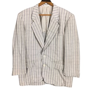 May include: A light-colored blazer with a grid pattern of thin blue lines. The blazer has a notched lapel, two front pockets, and two white buttons. It is hanging on a wooden hanger.