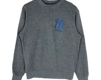 May include: A gray crew neck sweatshirt with the New York Yankees logo in blue on the chest. The logo includes the letters "NY" intertwined, with the word "Yankees" below. The sweatshirt has long sleeves and ribbed cuffs and hem.