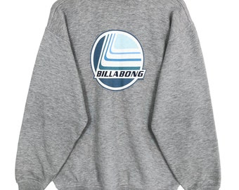 May include: A heather gray sweatshirt with a round logo on the back. The logo features a blue and white design with the word "BILLABONG" in a white font. The sweatshirt is hanging on a wooden hanger.