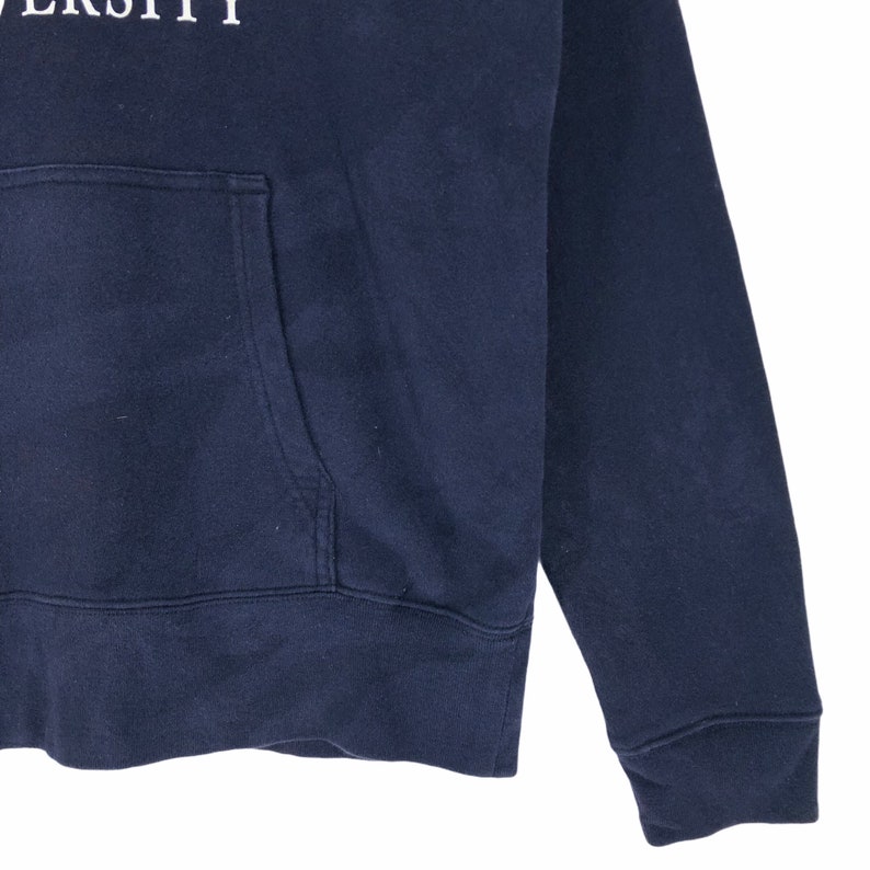 May include: Navy blue hooded sweatshirt with a front pocket. The sweatshirt has the word "UNIVERSITY" printed in white across the top. The sleeve and bottom hem are ribbed.