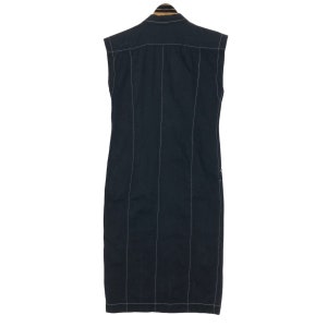 May include: A sleeveless, dark navy blue dress with vertical white stitching. The dress has a collared neckline and a button-down front. The back of the dress is visible, showcasing the tailored design and the contrasting white stitching.
