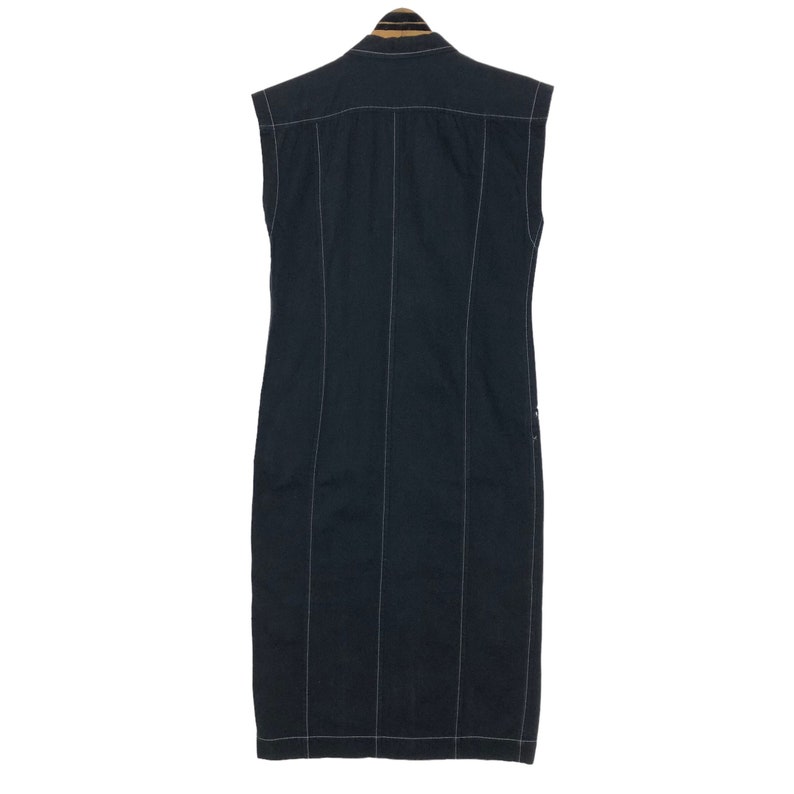 May include: A sleeveless, dark navy blue dress with vertical white stitching. The dress has a collared neckline and a button-down front. The back of the dress is visible, showcasing the tailored design and the contrasting white stitching.