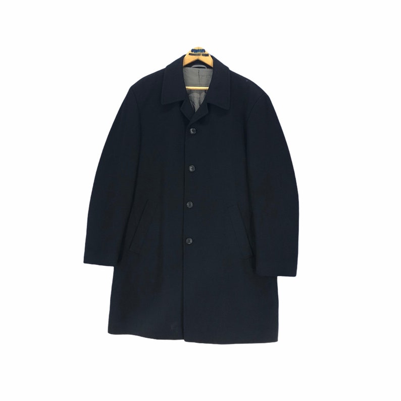 May include: A navy blue overcoat with a classic design. The coat features a button-up front, a notched collar, and two front pockets. It is hanging on a wooden hanger against a white background.