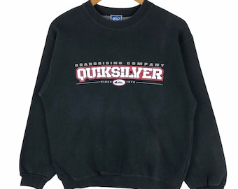 May include: Black crew neck sweatshirt with the text "BOARDRIDING COMPANY QUIKSILVER SINCE 1978" in white and red lettering. The sweatshirt is hanging on a wooden hanger.