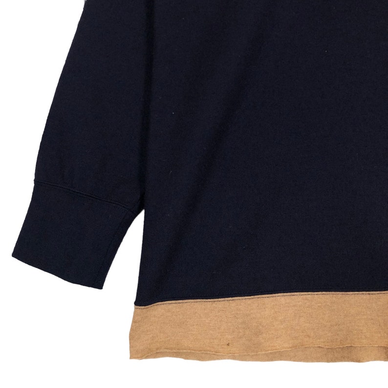 May include: A navy blue sweatshirt with a tan bottom hem and short sleeves. The sleeves have a wide cuff. The sweatshirt is made of a soft material.