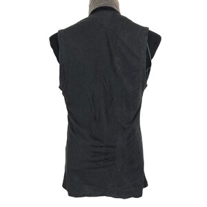May include: A dark gray vest with a V-neck collar. The vest is sleeveless and appears to be made of a soft, textured fabric. The back of the vest is visible, and it is displayed on a black mannequin.