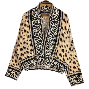 May include: A tan and black patterned jacket with a unique design. The jacket features a leopard print pattern with black and white geometric accents. The jacket has a button closure and a collared neckline. The jacket's design is eye-catching and stylish.