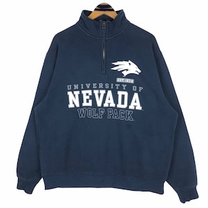 May include: Navy blue University of Nevada Wolf Pack sweatshirt with a quarter-zip collar. The white graphic features a wolf head and the text "UNIVERSITY OF NEVADA WOLF PACK" with "EST. 1874". The sweatshirt is hanging on a wooden hanger.