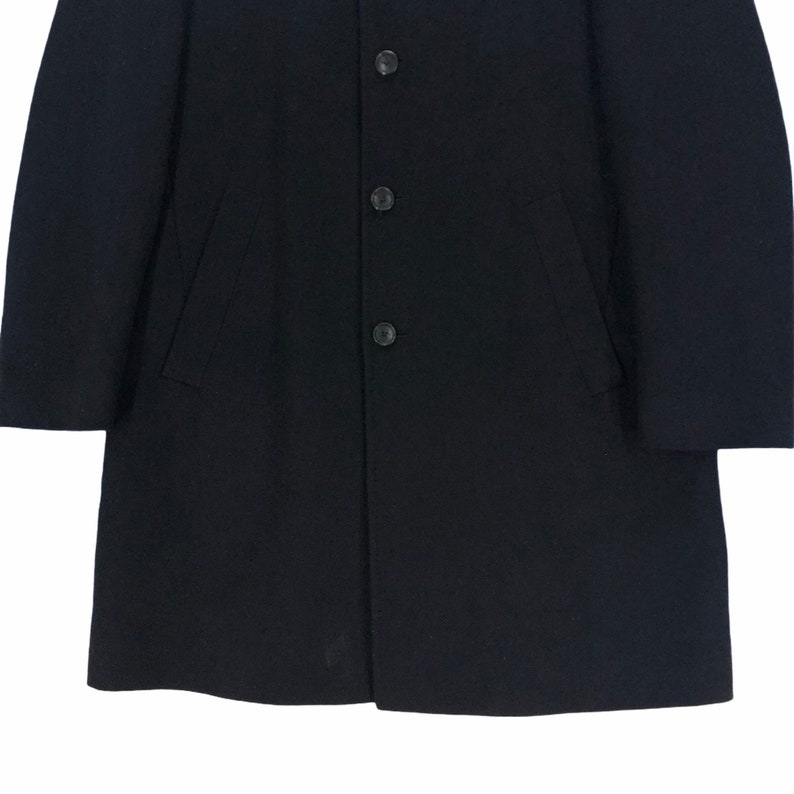 May include: A black overcoat with a classic design. The coat features a button-up front with three buttons and two side pockets. The coat's fabric appears to be a smooth, solid color, suitable for various occasions.