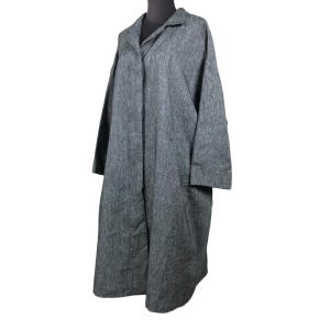 Pode incluir: Um casaco comprido cinzento com gola e mangas compridas. O casaco tem um corte folgado e dois bolsos grandes. O tecido tem um aspeto texturizado. O casaco é exibido num manequim preto.