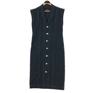 May include: A sleeveless, black dress with white stitching and a button-up front. The dress has a notched collar and two front pockets. The garment is hanging on a wooden hanger.