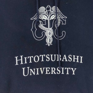 May include: Navy blue hooded sweatshirt featuring a white caduceus emblem and the text "Hitotsubashi University". The hoodie has a drawstring hood and is made of a soft material. The text is in a serif font.