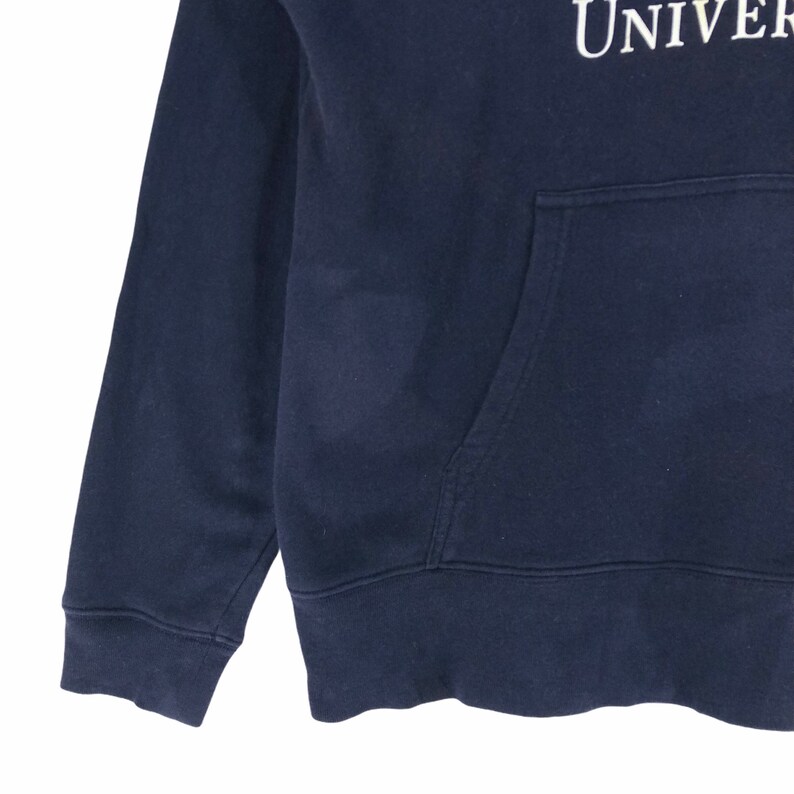 May include: Navy blue hooded sweatshirt with a front pocket. The sweatshirt has the word "UNIVER" printed in white on the upper right side. The cuffs and hem are ribbed.