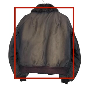 May include: A brown bomber jacket with a dark brown fur collar and a ribbed hem. The jacket is hanging on a hanger. The back of the jacket is visible.