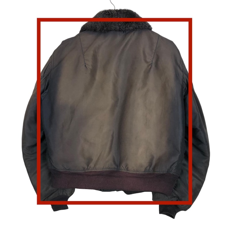May include: A brown bomber jacket with a dark brown fur collar and a ribbed hem. The jacket is hanging on a hanger. The back of the jacket is visible.