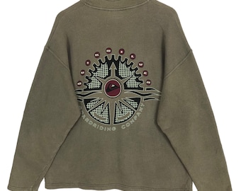 May include: A tan-colored sweatshirt with a high collar and long sleeves. The back features a large graphic of a compass rose with the text "QUIKSILVER RIDING COMPANY" in white. The graphic includes red, black, and white accents.