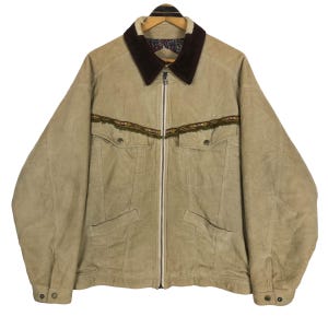 May include: Tan corduroy jacket with a dark brown collar and decorative trim across the chest. The jacket has a full zipper, two chest pockets, and two side pockets. The cuffs have button closures.