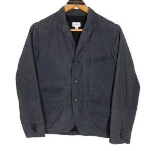 May include: A dark gray blazer with a subtle paisley pattern, three-button closure, and two front pockets. The jacket is hanging on a wooden hanger. The blazer has buttons on the sleeves.