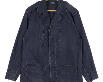 May include: A navy blue jacket with a collared neckline, two chest pockets, and two zippered pockets. The jacket has shoulder epaulets and is hanging on a wooden hanger. The brand name "A.P.C." is visible on the label.