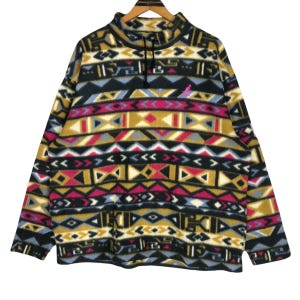 May include: A fleece pullover with a geometric pattern in black, yellow, pink, and blue. The long-sleeved top has a mock neck and a small pink kangaroo logo. The design features arrows, diamonds, and other shapes.
