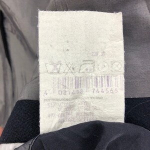 May include: A close-up of a clothing tag with a barcode and various symbols. The tag is white with black text and a purple barcode. The tag is attached to a dark garment.