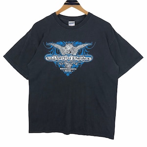 Può includere: T-shirt nera con il nome della band "Killswitch Engage" in bianco e blu, con un design stilizzato. Sotto il nome della band, il testo "Massachusetts Metal" è in blu. La maglietta è appesa a una gruccia di legno.