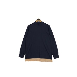 May include: A navy blue long-sleeve shirt with a mock neck and a tan-colored bottom hem. The shirt is hanging on a wooden hanger against a white background. The shirt is a solid color.