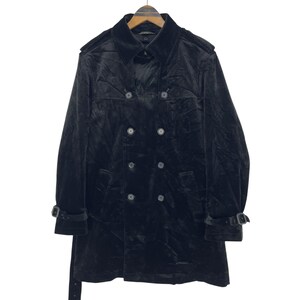 以下が含まれることがあります： 黒いベルベットのトレンチコート。ダブルブレストのデザインで、ノッチドラペル、肩のエポーレット、ベルトが付いています。袖にはバックル付きの調節可能な袖口が付いています。木製のハンガーにかかっています。