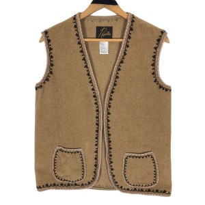May include: A tan vest with black, white, and orange decorative trim and two front pockets. The vest is hanging on a wooden hanger. The brand name "Needles" is visible on a tag.