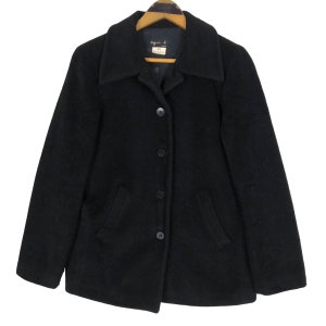 May include: A black wool coat with a classic collar and button-down closure. The coat has two front pockets and is hanging on a wooden hanger. The label reads "agnes b." and "40".