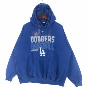 May include: A blue hooded sweatshirt with the text "Dodgers Baseball Los Angeles" in white. The sweatshirt has a front pocket and a drawstring hood. The Majestic logo is visible on the upper chest.