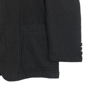 May include: Close-up of a black wool blazer. The blazer features a single pocket on the left side and three buttons on the sleeve. The fabric has a textured appearance.