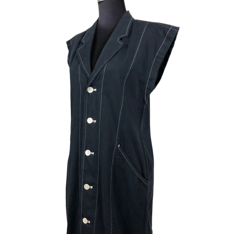 May include: A sleeveless black blazer-style dress with white vertical stitching and white buttons. The dress has a notched collar, a front pocket, and a tailored fit. The garment is displayed on a black mannequin.
