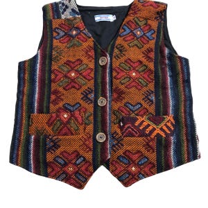 Peut inclure: Un gilet coloré à motifs avec un col en V et trois boutons en bois. Le gilet présente un motif géométrique dans les tons orange, rouge, bleu et vert, avec des accents rayés. Il possède deux poches avant et une doublure noire.