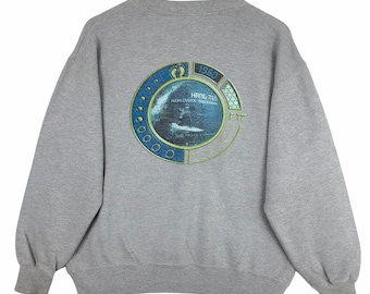 May include: A gray sweatshirt with a graphic on the back featuring the text "HANG TEN WORLDWIDE TRADEMARK" and the year "1960". The graphic is a circular design with blue and green accents, and a surfer on a wave.