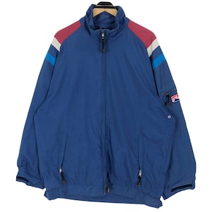 May include: A blue zip-up jacket with a high collar and a small logo on the sleeve. The jacket has red, white, and blue accents on the shoulders. It features two front pockets and a full-length zip.