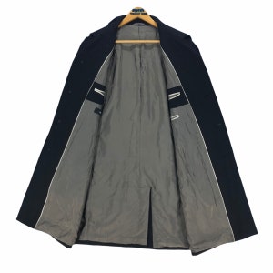 May include: A dark navy blue overcoat with a classic design. The coat is open, revealing a gray interior lining and white trim along the edges. The coat is hanging on a wooden hanger.
