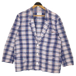 May include: A blue, white, and red plaid blazer with three white buttons and two front pockets. The blazer is hanging on a wooden hanger. The label reads "APEX GARDEN".