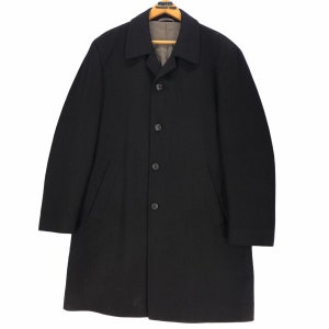 May include: A black overcoat with a notched collar, four buttons, and two front pockets. The coat is hanging on a wooden hanger. The lining is a light gray color.