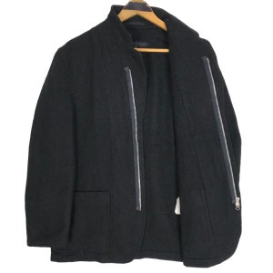 May include: Black jacket with a stand-up collar and two silver zippers running down the front. The jacket has two front pockets and is hanging on a wooden hanger. The jacket is made of a textured fabric.
