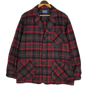 May include: A red, black, and gray plaid jacket with a collared neckline, three buttons, and two large front pockets. The jacket is hanging on a wooden hanger. The label on the jacket is visible.