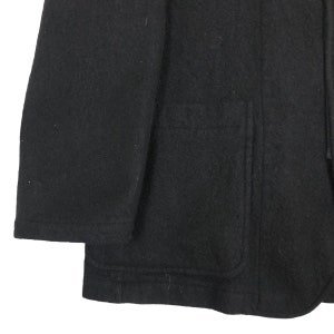 May include: A close-up of a black wool coat. The coat has a large pocket and a hood. The fabric appears to be thick and warm, suitable for cold weather. The coat is a solid black color.