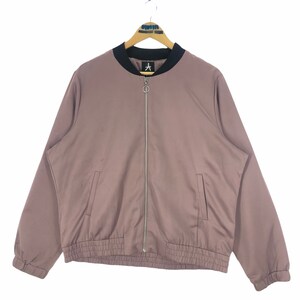 Könnte beinhalten: Mauvefarbene Bomberjacke mit schwarzem Kragen und silbernem Reißverschluss. Die Jacke hat zwei Vordertaschen und einen gerippten Saum und Bündchen. Ein kleines Logo ist auf der Brust zu sehen.