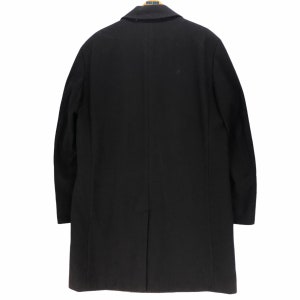 May include: A black overcoat with a notched lapel, hanging against a white background. The coat is a solid color, with a single vent in the back. The coat is made of a smooth, possibly wool, material.