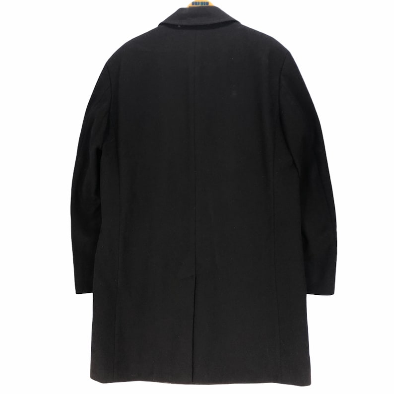 May include: A black overcoat with a notched lapel, hanging against a white background. The coat is a solid color, with a single vent in the back. The coat is made of a smooth, possibly wool, material.