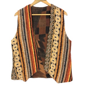 Könnte beinhalten: Eine Wendeweste mit einem lebendigen geometrischen Muster in Orange-, Schwarz-, Braun- und Gelbtönen. Die Weste ist ärmellos und hängt an einem Holzkleiderbügel vor einem weißen Hintergrund. Die Innenseite hat ein kontrastierendes braunes und schwarzes geometrisches Design.