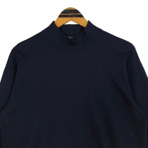 May include: A navy blue mock neck sweatshirt hanging on a wooden hanger. The sweatshirt has a high collar and long sleeves. The fabric appears to be a soft, comfortable material, suitable for casual wear.