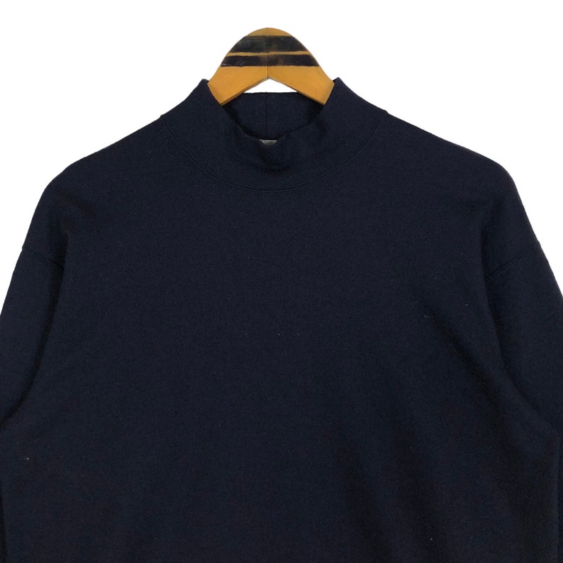 May include: A navy blue mock neck sweatshirt hanging on a wooden hanger. The sweatshirt has a high collar and long sleeves. The fabric appears to be a soft, comfortable material, suitable for casual wear.